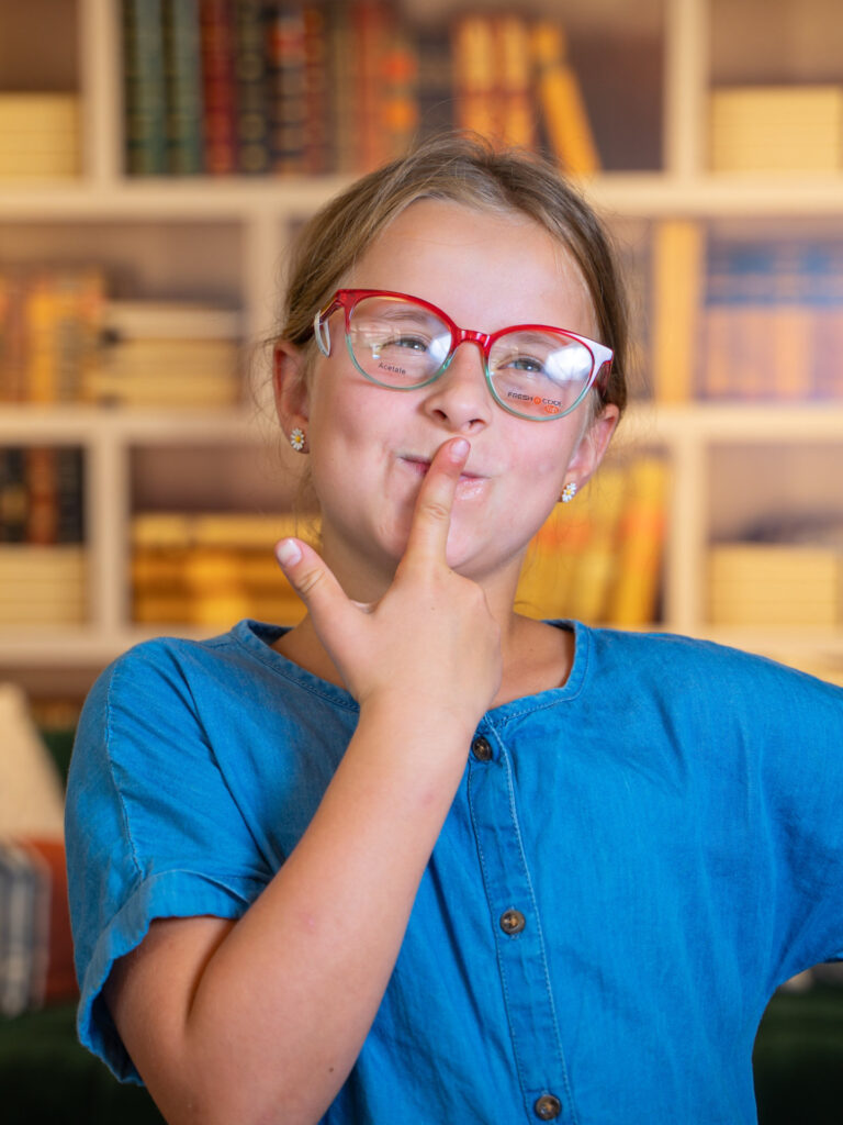 Kleines Mädchen mit roter Brille zeigt eine nachdenkliche Geste