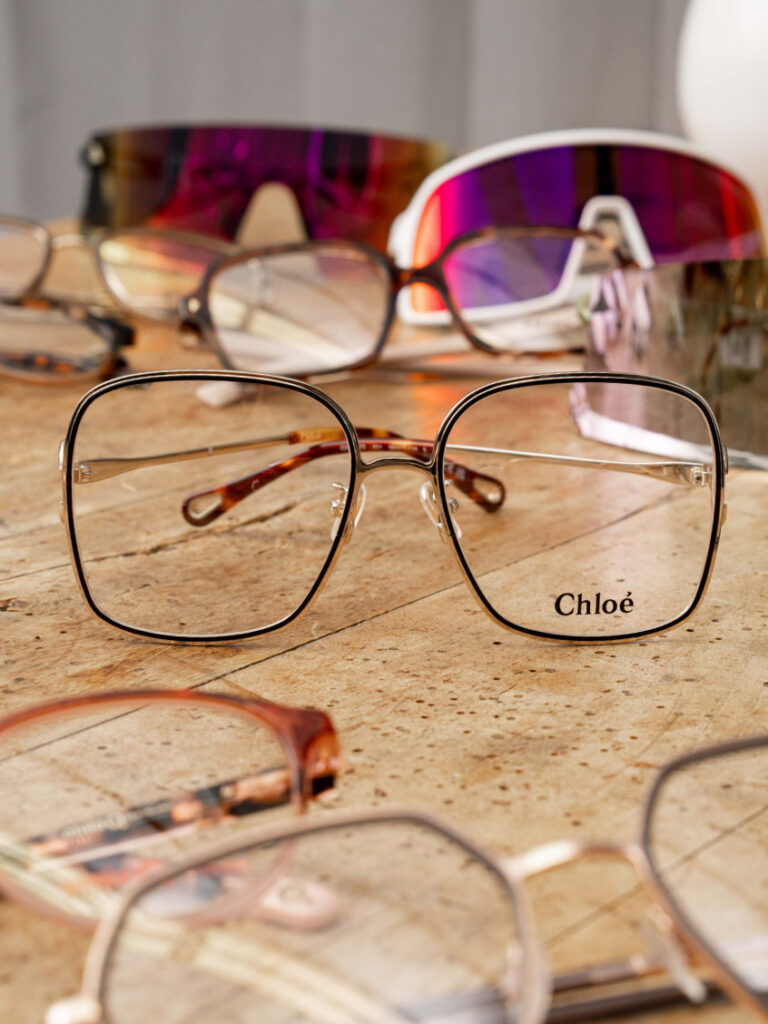 Mehrere Brillen auf einem Holztisch mit einer Brille mit großen Gläsern im Fokus in der Mitte