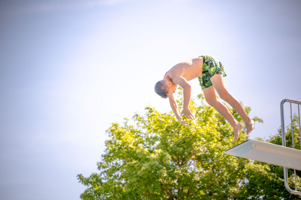 Ein junge der vom 3 Meterturm im Freibad einen Vorwärtssalt mache
