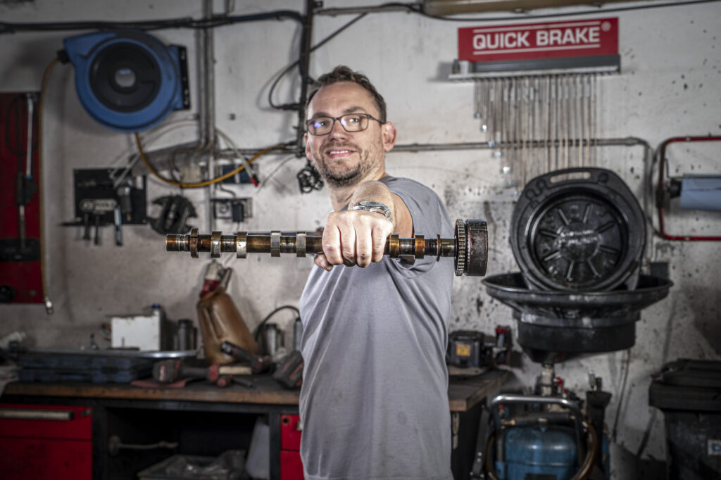 Mechaniker der eine Nockenwelle in der Hand hält