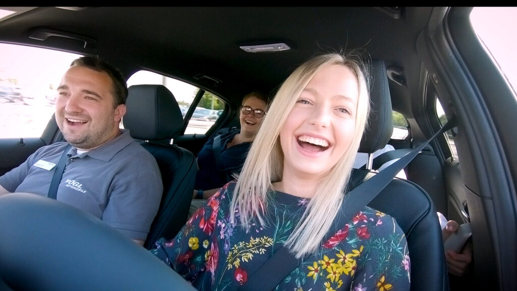 2 Frauen und ein Mann die in einem Auto sitzen und sichtlich Spaß am fahren haben.